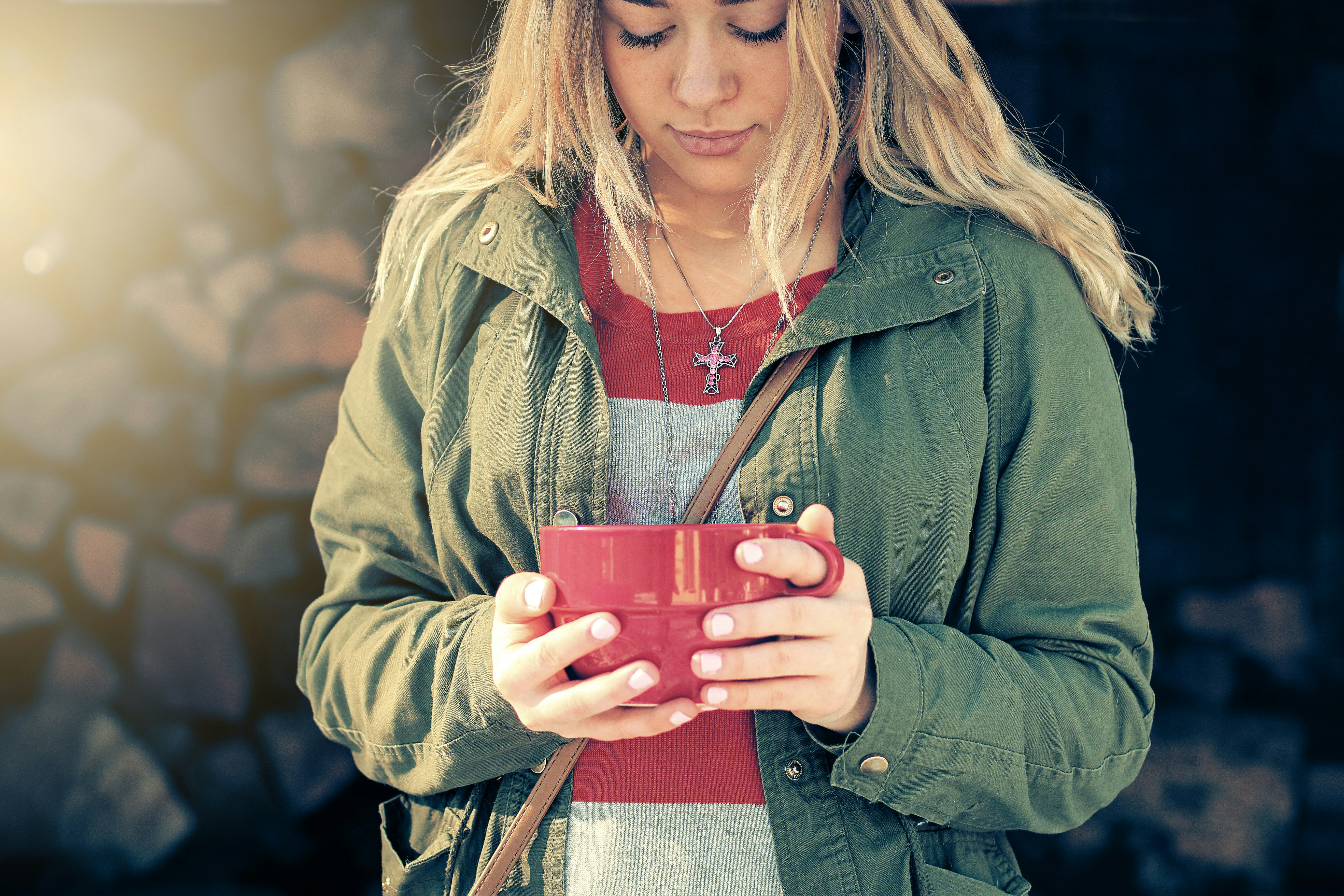 woman in green zip up jacket holding red ceramic mug